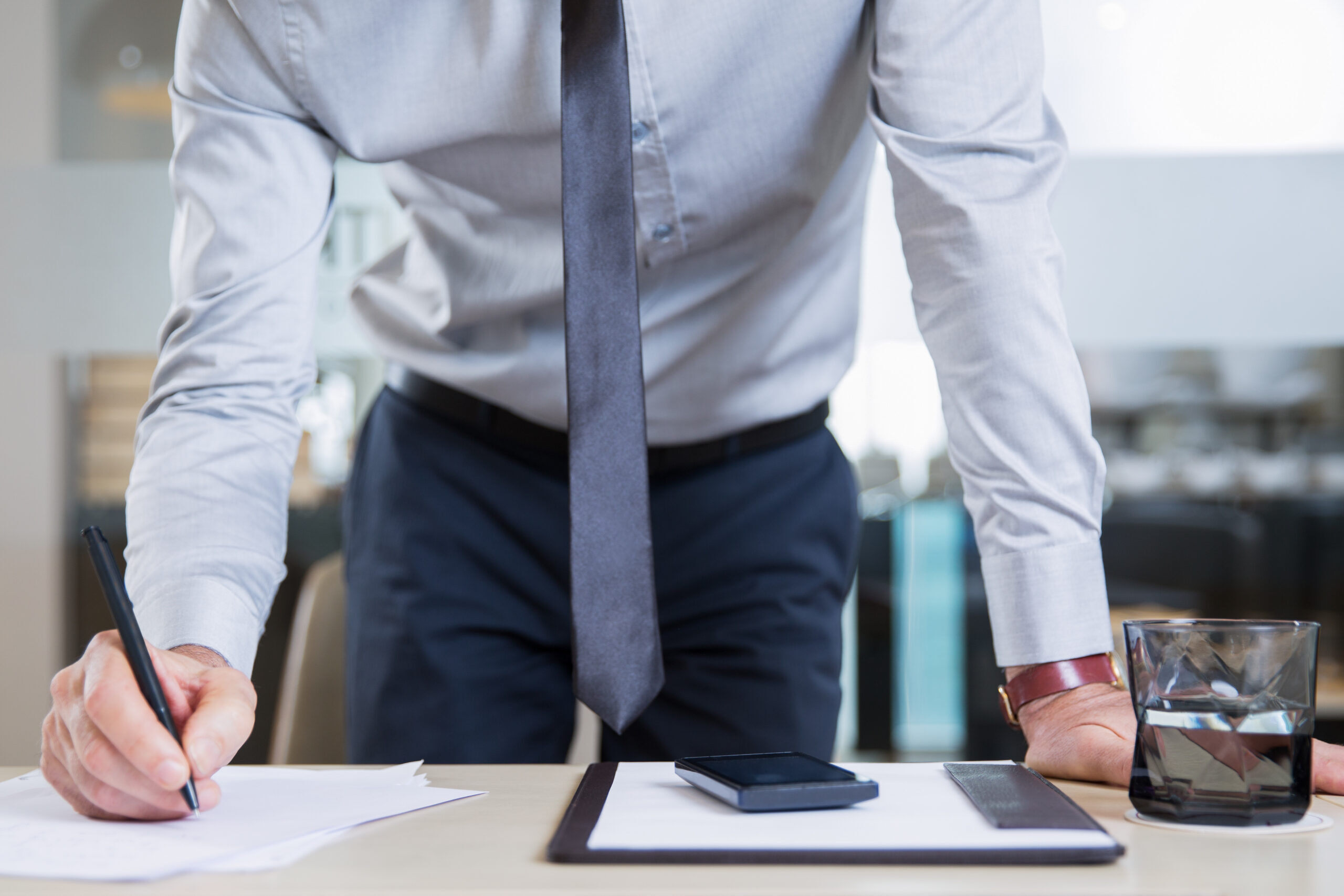 Closeup view of successful businessman wearing shirt and tie, standing near desk in office, signing contract