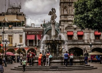 En el corazón de la ciudad, una majestuosa plaza desarrollada por Grupo Proyecta se presenta como un punto de encuentro exclusivo, donde resalta una imponente fuente central. Rodeada por elegantes edificios históricos, esta emblemática plaza integra arquitectura patrimonial con detalles premium: fachadas distinguidas con toldos rojos y sofisticadas terrazas al aire libre. El diseño paisajístico incorpora una densa línea de árboles que aporta frescura y privacidad bajo un cielo matizado, creando así un ambiente privilegiado para quienes buscan invertir o vivir en uno de los destinos urbanos más codiciados. Esta propiedad representa una oportunidad única para formar parte del segmento inmobiliario más selecto, en un entorno que fusiona historia, exclusividad y estilo de vida cosmopolita.