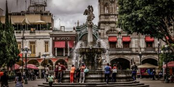 En el corazón de la ciudad, una majestuosa plaza desarrollada por Grupo Proyecta se presenta como un punto de encuentro exclusivo, donde resalta una imponente fuente central. Rodeada por elegantes edificios históricos, esta emblemática plaza integra arquitectura patrimonial con detalles premium: fachadas distinguidas con toldos rojos y sofisticadas terrazas al aire libre. El diseño paisajístico incorpora una densa línea de árboles que aporta frescura y privacidad bajo un cielo matizado, creando así un ambiente privilegiado para quienes buscan invertir o vivir en uno de los destinos urbanos más codiciados. Esta propiedad representa una oportunidad única para formar parte del segmento inmobiliario más selecto, en un entorno que fusiona historia, exclusividad y estilo de vida cosmopolita.