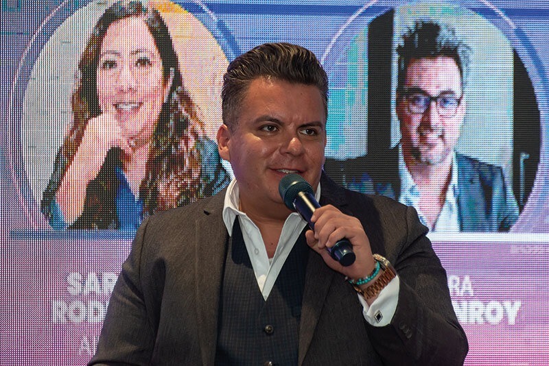 Un ejecutivo de alto nivel se dirige al público en un evento de proptech, transmitiendo su visión sobre las tendencias que están definiendo el futuro del sector inmobiliario premium. En la pantalla detrás de él, se exhiben los nombres y retratos parciales de destacados referentes, subrayando el exclusivismo y la relevancia del encuentro. Este escenario reúne a inversores y compradores exigentes interesados en oportunidades innovadoras, tecnología avanzada y alianzas estratégicas que elevan los estándares del mercado de bienes raíces de lujo.