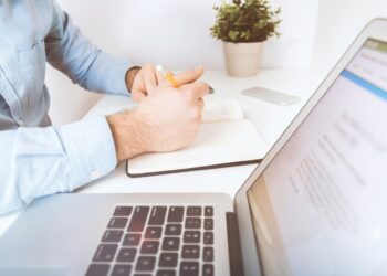 Un inversionista, vestido con una camisa azul claro, analiza detenidamente información clave en un escritorio minimalista y elegante. Frente a él, una computadora portátil abierta exhibe la plataforma Inmobot, herramienta líder en el sector inmobiliario premium para la gestión de oportunidades exclusivas. Junto a la tecnología de punta utilizada en el proceso de toma de decisión—smartphone y materiales cuidadosamente dispuestos—destaca el ambiente cómodo y eficiente que caracteriza a quienes apuestan por inversiones inmobiliarias de alto valor agregado.