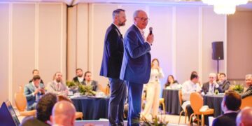 En el marco de un exclusivo evento organizado por Cushman & Wakefield, dos destacados profesionales del sector se posicionan en un elegante escenario. Uno de ellos, micrófono en mano, se dirige a una audiencia selecta compuesta por inversionistas y líderes del mercado inmobiliario premium, reunidos en un cómodo salón iluminado con calidez y dispuestos en mesas redondas. Este ambiente refleja la excelencia y distinción que caracteriza a los encuentros de alto nivel dedicados a las oportunidades más atractivas e innovadoras dentro del real estate de lujo.