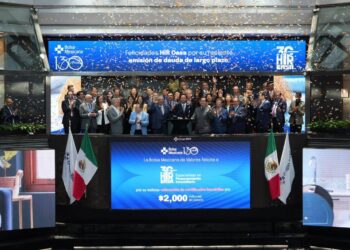 Un selecto grupo de profesionales del sector inmobiliario, elegantemente vestidos, se reúne en el escenario principal de la Bolsa Mexicana de Valores para celebrar un hito estratégico de HIR CASA. Flanqueados por dos banderas nacionales y bajo una lluvia de confeti, los líderes y socios clave comparten este momento trascendental mientras una pantalla proyecta mensajes de reconocimiento e información financiera relevante. Este evento simboliza la solidez, prestigio y proyección internacional que distingue a HIR CASA en el mercado inmobiliario premium, confirmando su atractivo incomparable para inversionistas acreedores y compradores exigentes que buscan oportunidades exclusivas con visión a futuro.