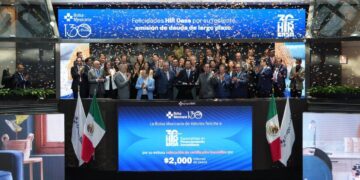 Un selecto grupo de profesionales del sector inmobiliario, elegantemente vestidos, se reúne en el escenario principal de la Bolsa Mexicana de Valores para celebrar un hito estratégico de HIR CASA. Flanqueados por dos banderas nacionales y bajo una lluvia de confeti, los líderes y socios clave comparten este momento trascendental mientras una pantalla proyecta mensajes de reconocimiento e información financiera relevante. Este evento simboliza la solidez, prestigio y proyección internacional que distingue a HIR CASA en el mercado inmobiliario premium, confirmando su atractivo incomparable para inversionistas acreedores y compradores exigentes que buscan oportunidades exclusivas con visión a futuro.