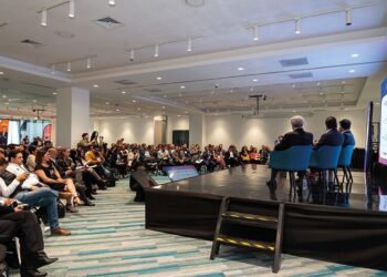 Un panel de expertos inmobiliarios se encuentra en el escenario, dirigiéndose a una audiencia selecta en un cómodo salón de conferencias. Los asistentes, atentos y comprometidos—muchos tomando notas y capturando imágenes clave—demuestran un interés genuino por las tendencias más exclusivas del sector. Una pantalla de gran formato acompaña la presentación, ofreciendo información relevante y actualizada sobre oportunidades de inversión premium, dinámicas del mercado y desarrollos emblemáticos para compradores e inversores que buscan excelencia y valor agregado en bienes raíces de alto nivel.