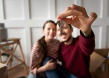 Una pareja sonriente sostiene un juego de llaves frente a la cámara, simbolizando la adquisición de su nueva residencia en México. Rodeados de mobiliario y cajas, celebran con satisfacción el acceso a una propiedad premium en un mercado inmobiliario de alta demanda y precios elevados. Este momento refleja las oportunidades únicas que ofrece el sector residencial exclusivo para quienes buscan invertir o establecerse en ubicaciones privilegiadas del país.
