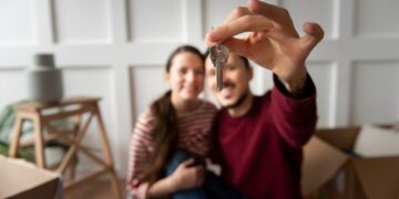 Una pareja sonriente sostiene un juego de llaves frente a la cámara, simbolizando la adquisición de su nueva residencia en México. Rodeados de mobiliario y cajas, celebran con satisfacción el acceso a una propiedad premium en un mercado inmobiliario de alta demanda y precios elevados. Este momento refleja las oportunidades únicas que ofrece el sector residencial exclusivo para quienes buscan invertir o establecerse en ubicaciones privilegiadas del país.
