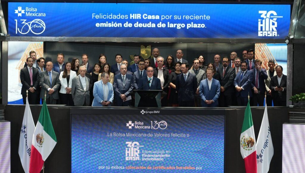Un selecto grupo de líderes empresariales se reúne en el escenario principal de la Bolsa Mexicana de Valores para celebrar la exitosa colocación de deuda a largo plazo por parte de Hir Casa. La ocasión fue resaltada por mensajes institucionales que reconocieron este hito estratégico, proyectados en pantallas ubicadas sobre y debajo del grupo. Este logro refuerza la solidez financiera y la visión innovadora de Hir Casa dentro del segmento inmobiliario premium, destacando su capacidad para generar valor sostenible e impulsar oportunidades exclusivas para inversionistas y compradores exigentes.