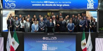 Un selecto grupo de líderes empresariales se reúne en el escenario principal de la Bolsa Mexicana de Valores para celebrar la exitosa colocación de deuda a largo plazo por parte de Hir Casa. La ocasión fue resaltada por mensajes institucionales que reconocieron este hito estratégico, proyectados en pantallas ubicadas sobre y debajo del grupo. Este logro refuerza la solidez financiera y la visión innovadora de Hir Casa dentro del segmento inmobiliario premium, destacando su capacidad para generar valor sostenible e impulsar oportunidades exclusivas para inversionistas y compradores exigentes.