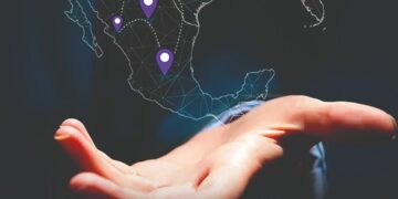 Se presenta una mano abierta en primer plano, debajo de un mapa digital de Norteamérica donde Múltiples pinos morados destacan ubicaciones estratégicas—con especial énfasis en el posicionamiento de México como epicentro del nearshoring. El fondo oscuro resalta la sofisticación del entorno, enfocando la atención tanto en las oportunidades geográficas clave como en el papel protagónico que México desempeña para inversionistas y compradores que buscan activos inmobiliarios premium vinculados a las tendencias globales del mercado.