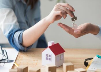 Una persona entrega la llave de una propiedad a otra, sobre una mesa con documentación, una maqueta residencial y bloques de madera. Esta escena representa el dinámico mercado inmobiliario premium en México, donde la activa demanda por inmuebles de alta gama evidencia el atractivo y solidez del sector para inversores y compradores beneficiosos que buscan activos exclusivos con alto potencial de valorización.