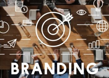 Una mesa de diseño elegante congrega a un selecto grupo de profesionales, cada uno de los cuales utiliza avanzados dispositivos electrónicos en un entorno que respira innovación y eficiencia. Sobre la imagen destacan iconos vinculados a la gestión de marca y el concepto "BRANDING" enfatizado por una imponente gráfica central de objetivo y flecha, símbolo de enfoque estratégico. Un ambiente ideal para inversores o compradores exigentes que valoran el trabajo colaborativo, la excelencia tecnológica y una visión clara orientada al éxito en el sector inmobiliario premium.