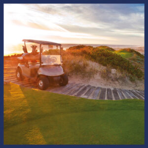Un exclusivo carrito de golf Moxi Global se encuentra estacionado sobre una elegante pasarela de madera, junto a un impecable campo de golf rodeado de dunas y vegetación autóctona. La escena, realzada por la luz dorada del atardecer, ofrece vistas panorámicas al océano y al horizonte, creando un entorno inigualable para quienes buscan invertir o residir en propiedades inmobiliarias premium con acceso directo a amenidades de primer nivel y paisajes excepcionales.