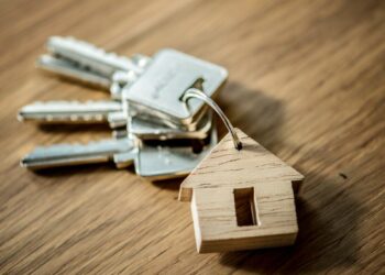 Juego de llaves metálicas en anilla, acompañado de un llavero en forma de casa elaborado en madera noble, elegantemente dispuesto sobre una superficie de fina madera. Un símbolo distintivo que representa acceso exclusivo a propiedades premium, diseñado para reflejar el estilo y la seguridad que buscan inversores y compradores exigentes en el sector inmobiliario de alto nivel.