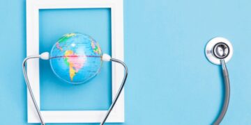 Un globo terráqueo en miniatura, delicadamente sostenido por un estetoscopio dentro de un marco blanco rectangular, destaca sobre un fondo azul claro. Esta imagen representa la visión global y el cuidado minucioso que definen a las inversiones inmobiliarias premium: seguridad, precisión y alcance internacional para satisfacer las expectativas de los compradores más exigentes.