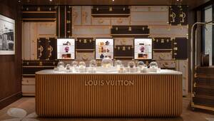 En un exclusivo espacio de exposición en Shanghái, Louis Vuitton presenta una cuidada selección de postres en cúpulas de cristal, dispuestos sobre un elegante mostrador claro que ostenta el distintivo sello de la casa. Al fondo, una pared decorada con los icónicos motivos de baúles clásicos y una sofisticada repisa boutique resaltan refinadas confecciones selectas en cajas, creando un ambiente que fusiona tradición y vanguardia. Esta propuesta no sólo subraya la atención al detalle y el diseño atemporal característicos de Louis Vuitton, sino que convierte cada elemento del espacio en una expresión tangible del lujo contemporáneo: atributos clave para quienes buscan invertir o adquirir propiedades alineadas con las más altas exigencias internacionales.