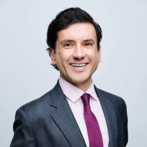 Un profesional de alta categoría, impecablemente vestido con un traje gris, camisa rosa claro y corbata con detalles en púrpura, posa con una actitud segura y cordial frente a un fondo neutro. Su imagen representa al Fideicomiso de Turismo de Los Cabos, una entidad clave en la promoción del destino más exclusivo de México. Este referente del sector inmobiliario premium encarna los valores de excelencia, confianza y visión internacional que exigen los inversores y compradores que buscan oportunidades excepcionales en uno de los mercados residenciales y turísticos más preferidos del país.