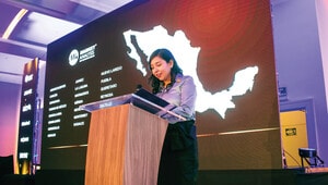 Una líder experta en análisis de mercado se dirige a una audiencia exclusiva durante un evento del sector inmobiliario premium. Desde el podio, presenta un estudio detallado sobre el desempeño y las oportunidades del sector industrial mexicano, mientras una pantalla de gran formato proyecta el mapa del país y las principales ciudades estratégicas para la inversión. El entorno cómodo y profesional, reforzado por una cuidada iluminación escénica, enfatiza la relevancia del foro para inversionistas y compradores que buscan información clave para la toma de decisiones enfocadas en activos inmobiliarios de alto valor en México.