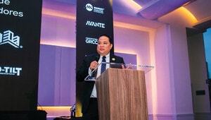 Un ejecutivo de alto nivel se dirige al sector industrial mexicano desde un elegante podio de acrílico, comunicando con claridad estrategias clave para el mercado inmobiliario premium. La atmósfera sofisticada del recinto y la proyección de logotipos corporativos refuerzan la relevancia del análisis de mercado en la toma de decisiones para inversionistas y compradores exigentes, destacando oportunidades exclusivas en un entorno dinámico y competitivo.