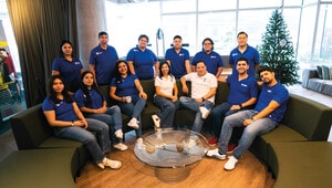 Un equipo de catorce profesionales, vestidos en elegantes tonos azul y blanco, se reúne en torno a un exclusivo sofá circular en el salón corporativo. Rodeados de una atmósfera sofisticada y detalles contemporáneos—como una mesa de centro de cristal y una decoración navideña selecta—analizan estrategias y tendencias del mercado inmobiliario premium. Este entorno promueve la colaboración estratégica entre especialistas dedicados a identificar oportunidades excepcionales para inversores y compradores que buscan activos inmobiliarios exclusivos.