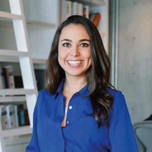 Una profesional de amplia trayectoria en el sector inmobiliario premium, reconocible por su elegante presencia y actitud acogedora, se encuentra en un entorno refinado—con estantes repletas de literatura especializada y un sobrio fondo gris. Ella está preparada para asesorarle sobre inversiones en exclusivos desarrollos hoteleros y estrategias avanzadas de financiamiento de proyectos. Su profundo conocimiento del mercado le garantiza una visión estratégica orientada a maximizar la rentabilidad y el valor patrimonial, proporcionando soluciones personalizadas para compradores e inversores con los más altos estándares de excelencia.