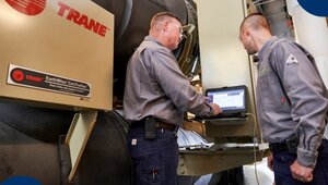 Dos técnicos especializados, uniformados y altamente calificados, supervisan detenidamente el funcionamiento de un avanzado sistema Trane EarthWise CenTraVac utilizando tecnología de monitoreo en tiempo real. Su labor meticulosa en el mantenimiento de sistemas de aire acondicionado garantiza eficiencia energética y optimización operativa, factores clave para empresas e inversores que buscan minimizar costos operativos y maximizar el rendimiento en propiedades inmobiliarias premium del sector industrial.