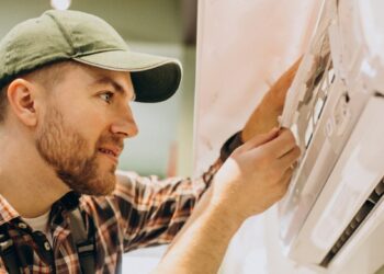 Un técnico especializado, debidamente uniformado, realiza una minuciosa inspección y ajuste en un sistema de aire acondicionado de pared de última generación. Este procedimiento garantiza el óptimo funcionamiento de los equipos, un factor esencial para mantener el alto estándar de confort climático esperado en residencias y propiedades premium. La calidad del mantenimiento técnico es clave para preservar tanto la eficiencia energética como la valorización a largo plazo de activos inmobiliarios exclusivos, asegurando así una experiencia superior para inversores y compradores exigentes.