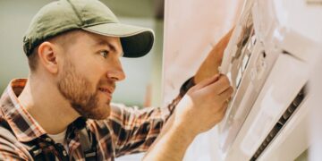 Un técnico especializado, debidamente uniformado, realiza una minuciosa inspección y ajuste en un sistema de aire acondicionado de pared de última generación. Este procedimiento garantiza el óptimo funcionamiento de los equipos, un factor esencial para mantener el alto estándar de confort climático esperado en residencias y propiedades premium. La calidad del mantenimiento técnico es clave para preservar tanto la eficiencia energética como la valorización a largo plazo de activos inmobiliarios exclusivos, asegurando así una experiencia superior para inversores y compradores exigentes.