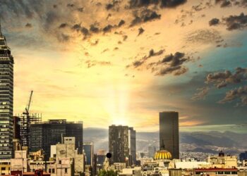 El horizonte urbano se presenta como un sofisticado equilibrio entre arquitectura contemporánea y patrimonio histórico, coronado al atardecer por la silueta imponente de un rascacielos emblemático en primer plano. Destaca la icónica estructura de cúpula dorada, símbolo del dinamismo y crecimiento sostenido de las FIBRAs en México, perfilándose como epicentro de las inversiones inmobiliarias premium. El entorno se realza con una vista majestuosa hacia las montañas y un cielo cautivador, evocando exclusividad y potencial de plusvalía para compradores e inversionistas que exigen excelencia arquitectónica y ubicaciones privilegiadas.