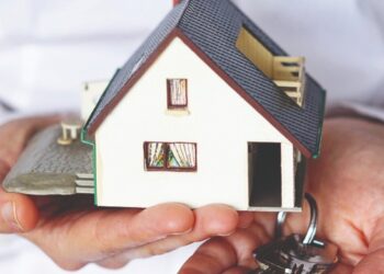 Una persona sostiene en una mano una elegante maqueta de residencia y en la otra un juego de llaves plateadas, representando el proceso exclusivo de adquisición o arrendamiento inmobiliario. La imagen enfatiza la importancia de comprender las obligaciones que recaen sobre los propietarios de bienes inmuebles en la Ciudad de México, conforme al artículo 132 del Código Fiscal local. Esta normativa resulta fundamental para inversores y compradores beneficiosos que buscan asegurar su bajo estándares legales sólidos y maximizar el valor de sus activos en el sector inmobiliario premium.