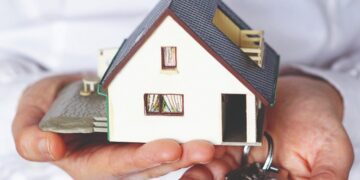 Una persona sostiene en una mano una elegante maqueta de residencia y en la otra un juego de llaves plateadas, representando el proceso exclusivo de adquisición o arrendamiento inmobiliario. La imagen enfatiza la importancia de comprender las obligaciones que recaen sobre los propietarios de bienes inmuebles en la Ciudad de México, conforme al artículo 132 del Código Fiscal local. Esta normativa resulta fundamental para inversores y compradores beneficiosos que buscan asegurar su bajo estándares legales sólidos y maximizar el valor de sus activos en el sector inmobiliario premium.
