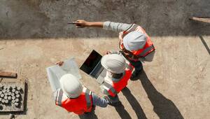 Tres profesionales de la construcción, equipados con cascos blancos y chalecos de alta visibilidad, supervisan el avance de la obra desde una perspectiva estratégica. Comprometidos con los más altos estándares de seguridad y excelencia, uno dirige la atención hacia áreas clave del desarrollo, mientras que otro gestiona datos e información técnica desde un portátil de última generación. El tercero analiza detalladamente los planos arquitectónicos, asegurando que cada detalle se ejecute conforme a las especificaciones premium que distinguen a este proyecto inmobiliario exclusivo.