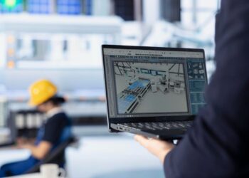 Una persona sostiene un portátil que exhibe un modelo 3D de una instalación industrial de última generación, ilustrando el avance hacia la transformación digital. En segundo plano, difuminado, se observa a un operario con casco de seguridad interactuando con maquinaria especializada en un entorno industrial moderno. Esta escena resalta la integración de tecnología de punta en espacios industriales premium—una propuesta ideal para inversores y compradores visionarios que buscan activos inmobiliarios diseñados para maximizar la eficiencia operativa, la innovación y el valor sostenido.