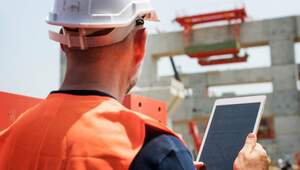 Un profesional equipado con casco blanco y chaleco naranja supervisa una obra en construcción en México, utilizando una tableta como herramienta principal de gestión. Esta escena ilustra la integración de tecnología avanzada y transformación digital aplicada al sector inmobiliario premium, asegurando altos estándares de eficiencia y control en cada etapa del desarrollo. La estructura de concreto parcialmente edificada al fondo refleja el compromiso con proyectos innovadores que cumplen las expectativas más exigentes de inversionistas y compradores selectos.