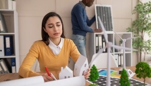 En un entorno corporativo de alto nivel, una profesional supervisa maquetas arquitectónicas que integran viviendas exclusivas con tecnologías avanzadas como paneles solares y aerogeneradores, evidenciando un enfoque innovador en diseño sostenible. Al fondo, otro especialista evalúa soluciones fotovoltaicas, reafirmando el compromiso de la firma con desarrollos inmobiliarios premium orientados a la eficiencia energética y la inversión responsable.