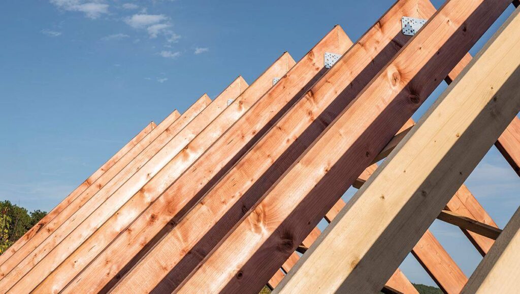 Vista detallada de las cerchas de madera bajo construcción, enmarcadas contra un cielo despejado. Las vigas—perfectamente alineadas y aseguradas con placas metálicas—evidencian prácticas constructivas sostenibles y duraderas. Esta meticulosa atención a la calidad estructural garantiza una inversión segura y atractiva para quienes buscan excelencia arquitectónica en el mercado inmobiliario premium.