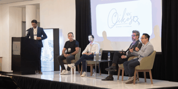 Cinco destacados profesionales del sector lideran un panel enfocado en innovación proptech y digitalización inmobiliaria, abordando tendencias clave que transforman el mercado premium. Un ponente principal expone desde el podio, mientras cuatro expertos debaten con micrófono en mano, aportando perspectivas estratégicas para inversores y compradores de alto perfil. De fondo, la pantalla resalta el patrocinio Gold y exhibe con distinción la marca ABC Cikos, subrayando la exclusividad y relevancia del evento.