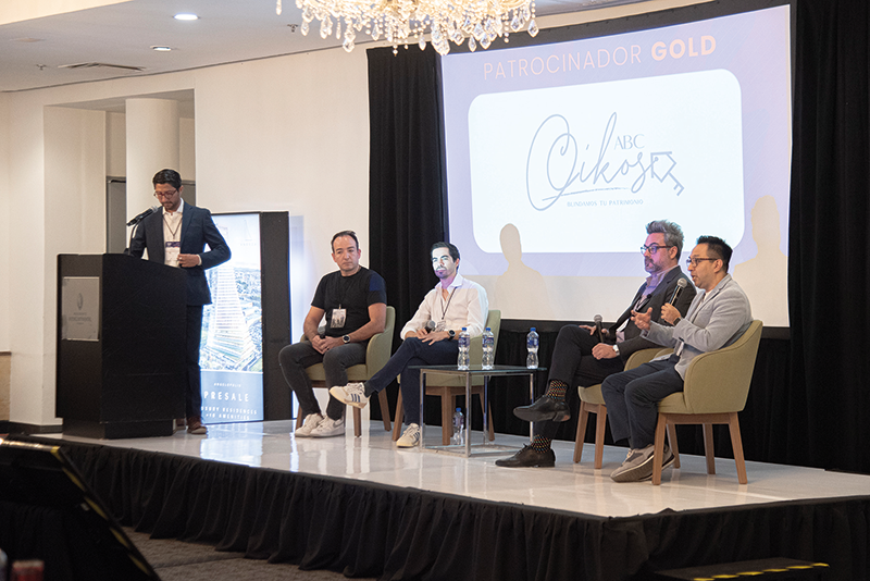 Cinco destacados profesionales del sector lideran un panel enfocado en innovación proptech y digitalización inmobiliaria, abordando tendencias clave que transforman el mercado premium. Un ponente principal expone desde el podio, mientras cuatro expertos debaten con micrófono en mano, aportando perspectivas estratégicas para inversores y compradores de alto perfil. De fondo, la pantalla resalta el patrocinio Gold y exhibe con distinción la marca ABC Cikos, subrayando la exclusividad y relevancia del evento.