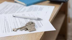 Sobre una elegante mesa de madera, un juego de llaves con llavero en forma de casa, acompañado por un bolígrafo y documentos relativos a fraudes contra arrendadores, reflejan la importancia de la seguridad jurídica en el sector inmobiliario premium. Al fondo, un libro azul subraya los retos y oportunidades presentes en el dinámico mercado de vivienda en renta en México, enfatizando la necesidad de soluciones confiables para inversionistas y compradores que buscan proteger su patrimonio y maximizar su retorno.