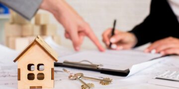 Sobre una mesa, un modelo arquitectónico en madera y llaves se disponen junto a documentos oficiales. Al fondo, dos personas revisan detenidamente los términos contractuales, enfatizando la formalidad y confianza del proceso de inversión inmobiliaria. Esta escena refleja el dinamismo actual del mercado premium de vivienda en renta en México, donde cada detalle es gestionado con rigor profesional para garantizar seguridad jurídica y sólidas oportunidades de retorno para compradores e inversionistas exigentes.