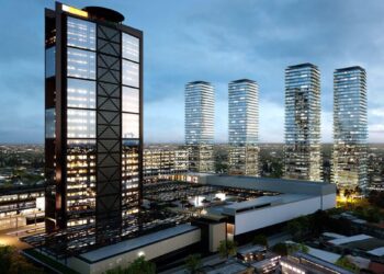 Un dinámico horizonte urbano al anochecer destaca una imponente torre de oficinas, cuyas ventanas iluminadas revelan la actividad empresarial de alto nivel, en conjunto con cuatro elegantes residencias verticales de cristal. Estas edificaciones premium reflejan la consolidación y el crecimiento sostenido de la representación inmobiliaria en mercados exclusivos. El entorno se complementa con edificaciones menores y un cuidadoso trazado vial, subrayando el desarrollo estratégico y moderno del sector para inversores y compradores que buscan ubicaciones privilegiadas, arquitectura vanguardista y alta plusvalía.