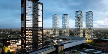 Un dinámico horizonte urbano al anochecer destaca una imponente torre de oficinas, cuyas ventanas iluminadas revelan la actividad empresarial de alto nivel, en conjunto con cuatro elegantes residencias verticales de cristal. Estas edificaciones premium reflejan la consolidación y el crecimiento sostenido de la representación inmobiliaria en mercados exclusivos. El entorno se complementa con edificaciones menores y un cuidadoso trazado vial, subrayando el desarrollo estratégico y moderno del sector para inversores y compradores que buscan ubicaciones privilegiadas, arquitectura vanguardista y alta plusvalía.