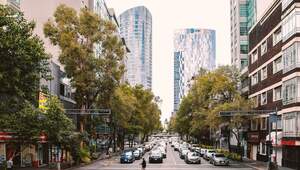 Una vibrante avenida flanqueada por elegantes automóviles y árboles urbanos se integra armoniosamente con edificaciones de media y gran altura. Destacan dos rascacielos de diseño contemporáneo en vidrio, símbolos del crecimiento vertical y la sofisticación arquitectónica que definen a las principales ciudades de México. Este entorno dinámico urbano, resaltado por Propiedades.com, refleja el auge del sector inmobiliario premium, presentando oportunidades excepcionales para inversionistas y compradores que buscan exclusividad, modernidad y alta plusvalía.