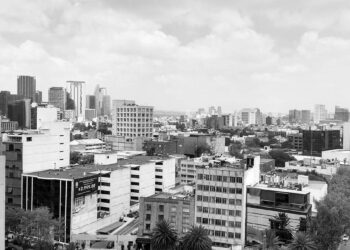 Fotografía en blanco y negro de un paisaje urbano dominado por imponentes rascacielos y elegantes edificios de media altura, reflejando el proceso de transformación que define las principales ciudades de México. La imagen captura un entorno metropolitano denso y cómodo, bajo un cielo nublado, donde la modernización continua ofrece oportunidades exclusivas para inversionistas exigentes que buscan participar en el desarrollo inmobiliario premium.