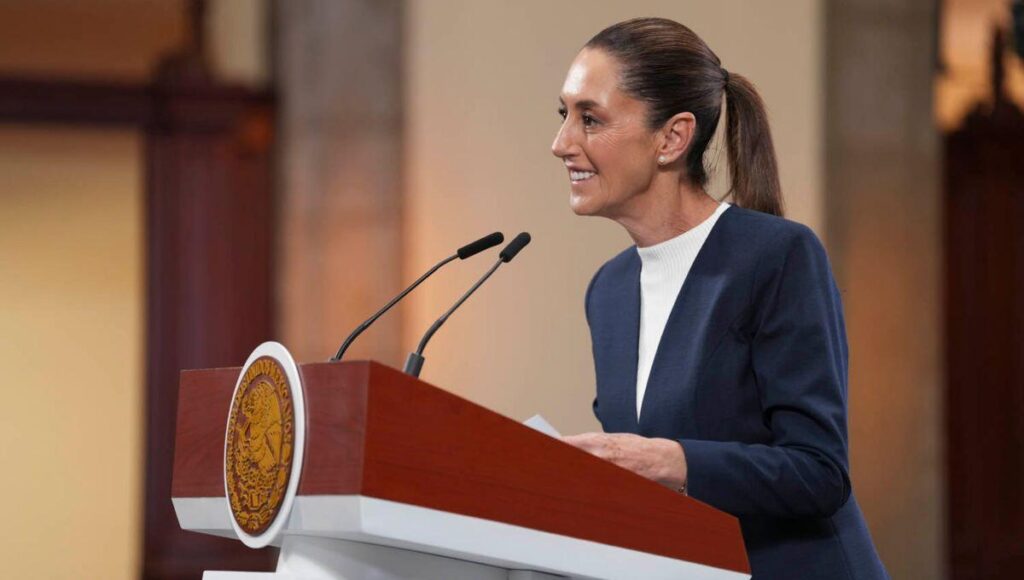 Una mujer elegantemente vestida con un blazer azul marino se posiciona al frente de un podio institucional, equipado con micrófonos, transmitiendo seguridad y liderazgo en su discurso. El distintivo sello oficial del podio refleja la trascendencia del acontecimiento, mientras que el entorno, cuidadosamente presentado, denota la exclusividad de un evento vinculado a Infonavit. La escena proyecta profesionalismo y compromiso absoluto con estándares de excelencia, elementos clave para quienes buscan invertir o adquirir propiedades premium en el sector inmobiliario.
