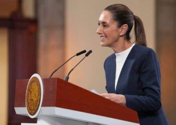 Una mujer elegantemente vestida con un blazer azul marino se posiciona al frente de un podio institucional, equipado con micrófonos, transmitiendo seguridad y liderazgo en su discurso. El distintivo sello oficial del podio refleja la trascendencia del acontecimiento, mientras que el entorno, cuidadosamente presentado, denota la exclusividad de un evento vinculado a Infonavit. La escena proyecta profesionalismo y compromiso absoluto con estándares de excelencia, elementos clave para quienes buscan invertir o adquirir propiedades premium en el sector inmobiliario.