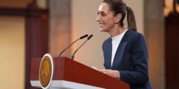 Una mujer elegantemente vestida con un blazer azul marino se posiciona al frente de un podio institucional, equipado con micrófonos, transmitiendo seguridad y liderazgo en su discurso. El distintivo sello oficial del podio refleja la trascendencia del acontecimiento, mientras que el entorno, cuidadosamente presentado, denota la exclusividad de un evento vinculado a Infonavit. La escena proyecta profesionalismo y compromiso absoluto con estándares de excelencia, elementos clave para quienes buscan invertir o adquirir propiedades premium en el sector inmobiliario.