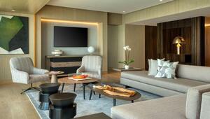 Sofisticada sala de estar con una paleta de tonos neutros, que incorpora un sofá beige, elegantes butacas tapizadas a rayas y mesas de centro circulares. El arte abstracto en las paredes y los detalles en madera realzan el ambiente, ofreciendo una atmósfera contemporánea y acogedora, ideal para quienes valoran la exclusividad y el confort características del sector inmobiliario premium en Lima, Perú. Un delicado arreglo de orquídea blanca aporta un toque distintivo al espacio, reflejando los más altos estándares de diseño presentes en residencias o propiedades a la altura de los principales hoteles de lujo internacionales.