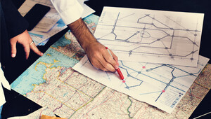 Una persona señala con un bolígrafo rojo un plano impreso del sistema de transporte urbano, mientras en la mesa se despliegan mapas viales y globales. El equipo analiza estratégicamente los posibles riesgos asociados a una ubicación subóptima para proyectos de nearshoring. Este enfoque minucioso garantiza que cada decisión inmobiliaria se base en conectividad privilegiada, accesibilidad internacional y el máximo potencial de crecimiento, elementos fundamentales para inversionistas y compradores que buscan activos premium.