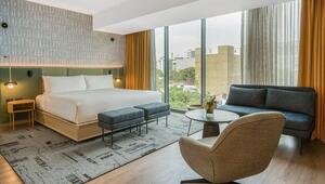 Exclusiva suite de hotel en Lima, diseñada para el sector inmobiliario premium. Esta elegante habitación cuenta con una imponente cama king size, dos bancos auxiliares y un área de descanso equipada con sofá azul, mesa redonda y silla. Sus ventanas de piso a techo, vestidos con cortinas amarillas, permiten disfrutar de vistas panorámicas a la ciudad. Una oportunidad única que redefine el lujo urbano y asegura una experiencia incomparable para inversores o compradores que buscan distinción y valor sustentable en los hoteles IHG más exclusivos.